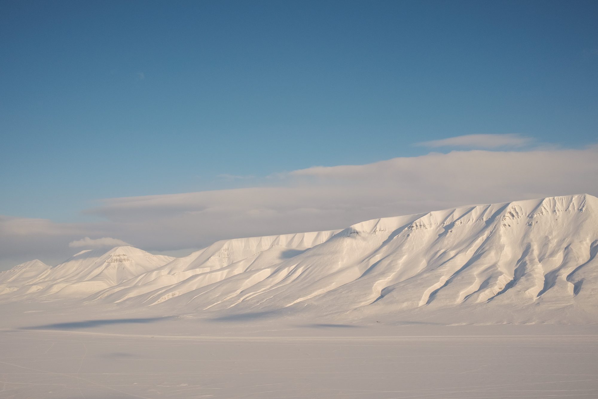 Snow-covered mountains in first light, a band of cloud resting on the ridges.